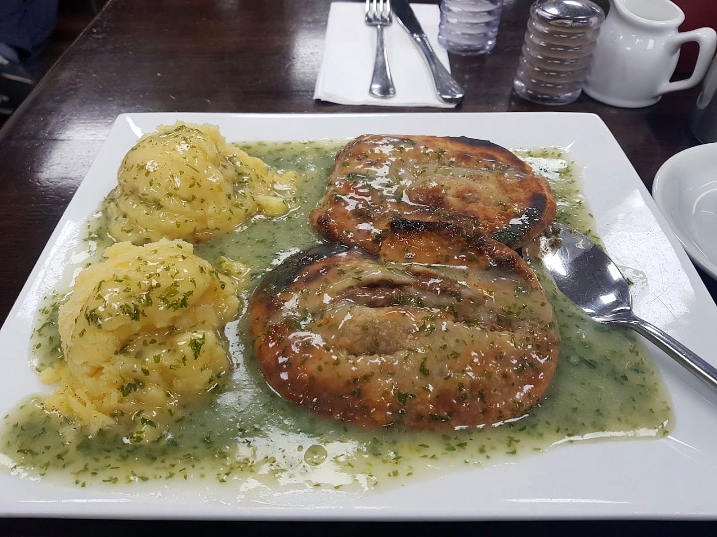 Two pies with mashed potato and green parsley liquor on a white plate