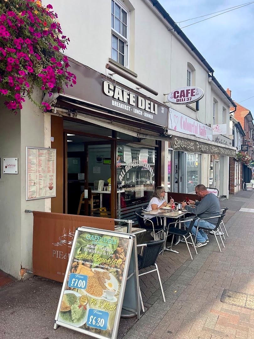 Cafe Deli on Billericay High Street: dark fascia with white lettering, an oval hanging sign, pink hanging baskets and tables on the pavement